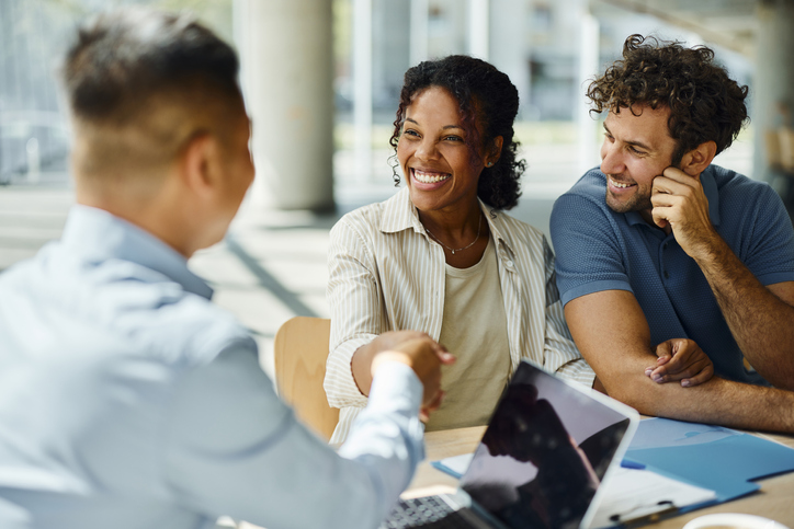 A couple sitting at a table with a bank employee, with the woman shaking the employee's hand.