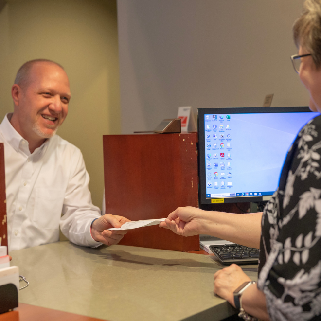 A bank teller handing a man a piece of paper.