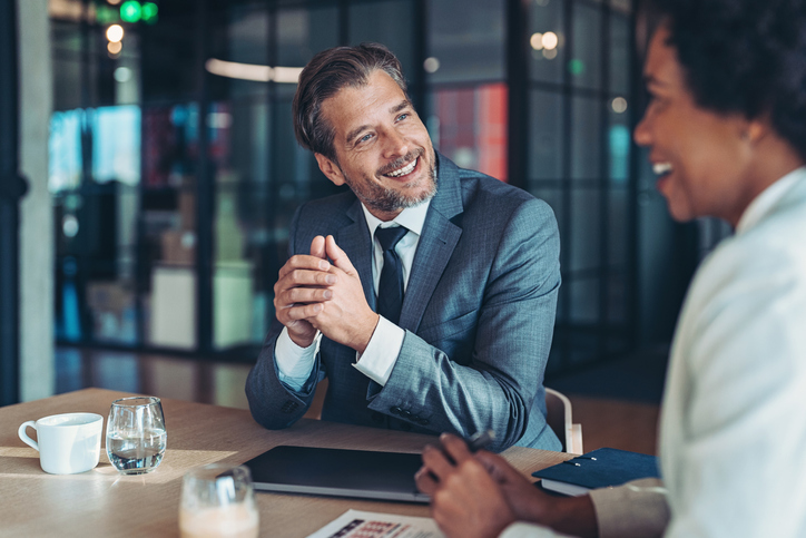 Two people sitting at a table and the man is smiling at the woman.